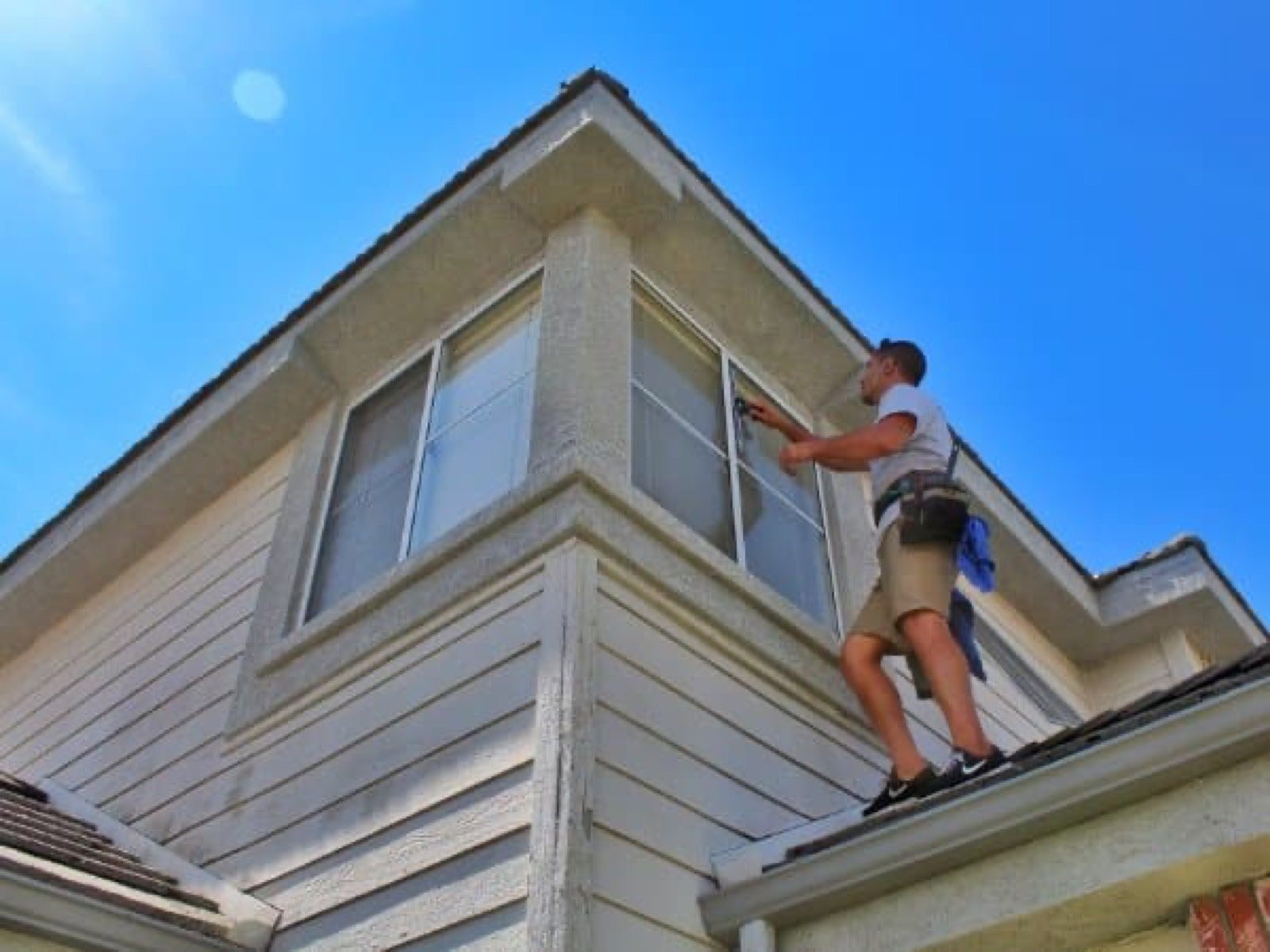 Technician cleaning a home's upper exterior from the roof